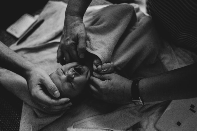 Geburtsfotografie Allgäu Baby wird das erste Mal nach der Geburt untersucht und gähnt bei Geburtsreportage in München